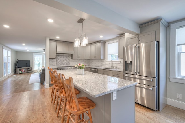 kitchen with sink, hanging light fixtures, light stone counters, a kitchen island, and appliances with stainless steel finishes