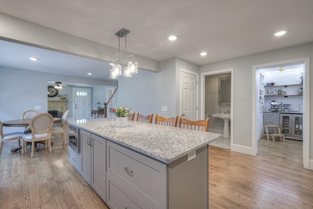 kitchen with gray cabinetry, a center island, hanging light fixtures, light wood-type flooring, and light stone counters