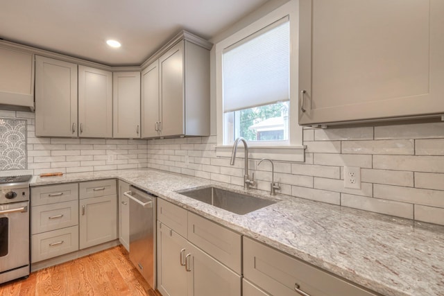 kitchen featuring light stone countertops, appliances with stainless steel finishes, tasteful backsplash, sink, and light hardwood / wood-style flooring