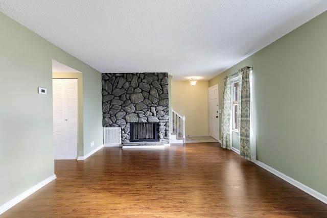 unfurnished living room featuring a stone fireplace, wood-type flooring, and a textured ceiling