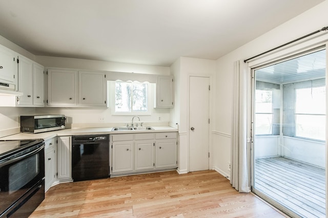 kitchen with sink, black appliances, light hardwood / wood-style flooring, white cabinets, and range hood