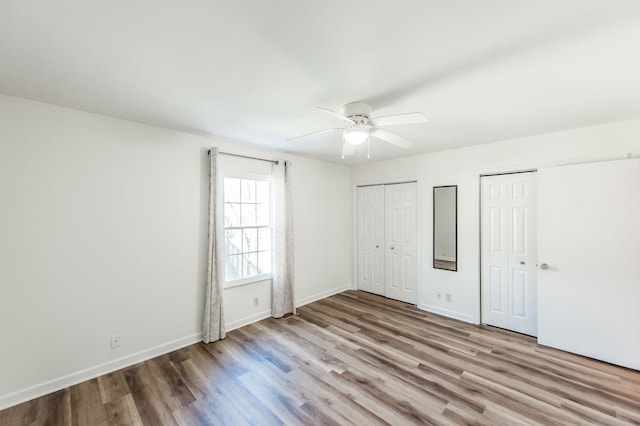 unfurnished bedroom with light hardwood / wood-style flooring, ceiling fan, and multiple closets