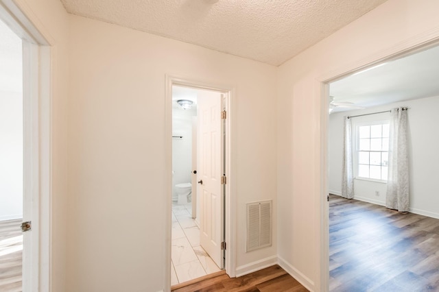 hall featuring light wood-type flooring and a textured ceiling