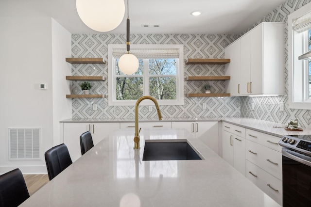 kitchen featuring white cabinetry, hanging light fixtures, stainless steel range with electric stovetop, and sink