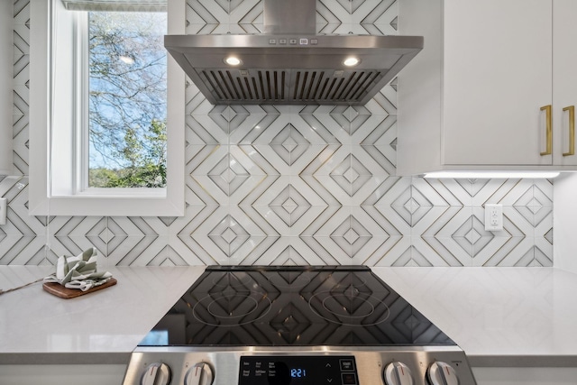 kitchen with tasteful backsplash, white cabinets, and wall chimney range hood