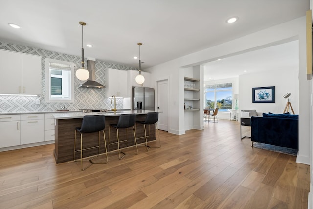 kitchen with stainless steel fridge with ice dispenser, a center island, white cabinetry, and wall chimney exhaust hood