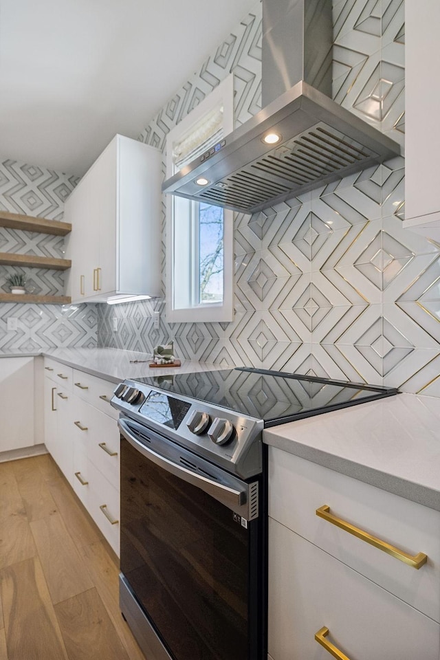 kitchen with light wood-type flooring, tasteful backsplash, ventilation hood, electric stove, and white cabinets