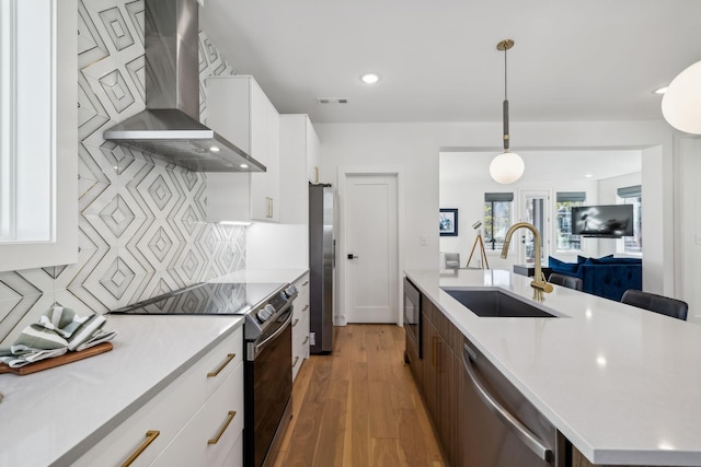 kitchen featuring white cabinetry, sink, wall chimney range hood, pendant lighting, and appliances with stainless steel finishes