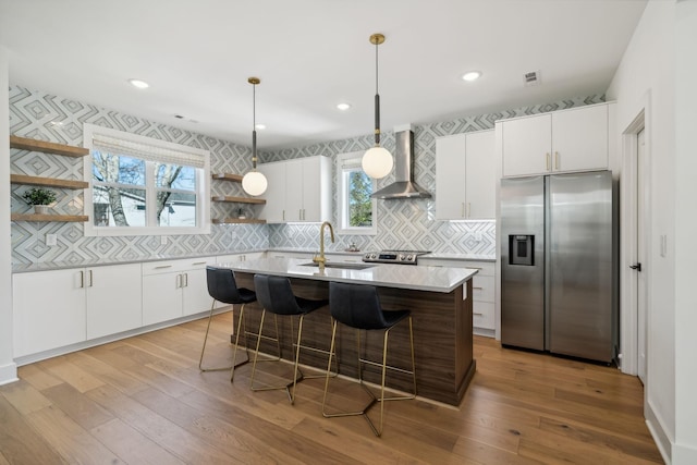 kitchen featuring white cabinets, sink, wall chimney exhaust hood, an island with sink, and appliances with stainless steel finishes