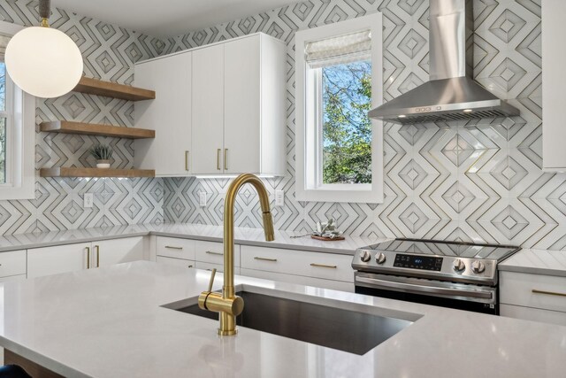 kitchen featuring sink, wall chimney exhaust hood, pendant lighting, stainless steel range with electric stovetop, and white cabinets