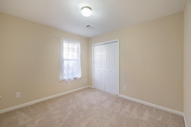 unfurnished bedroom with light colored carpet and a closet