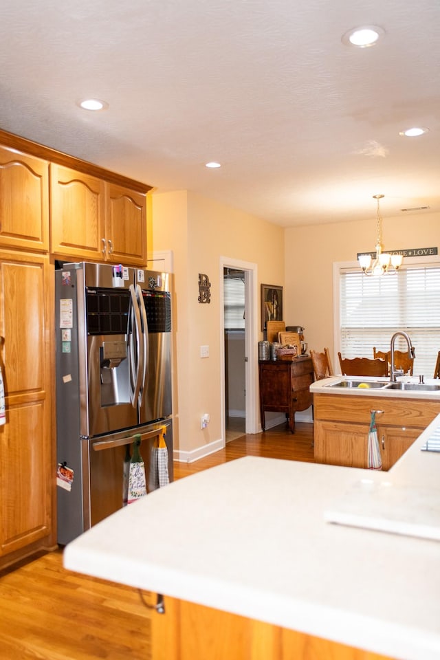 kitchen featuring decorative light fixtures, light wood-type flooring, a notable chandelier, stainless steel refrigerator, and sink