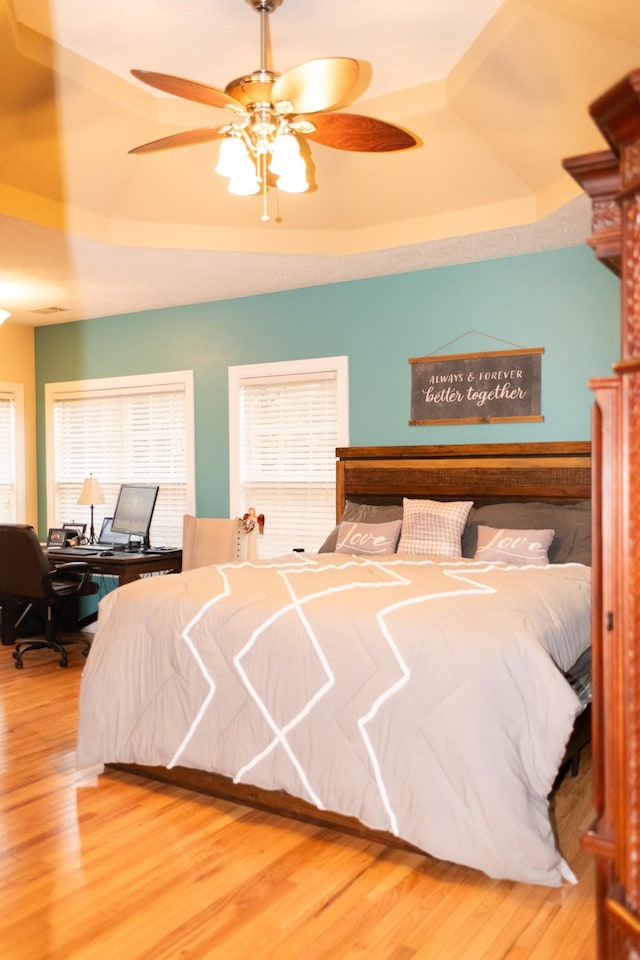 bedroom with ceiling fan, a raised ceiling, and hardwood / wood-style flooring