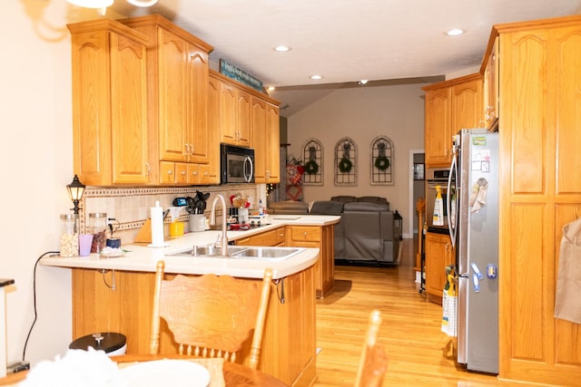 kitchen featuring tasteful backsplash, kitchen peninsula, a kitchen bar, light wood-type flooring, and appliances with stainless steel finishes