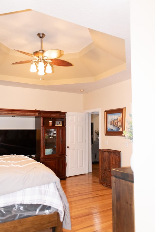 bedroom featuring a raised ceiling, ceiling fan, and light hardwood / wood-style floors