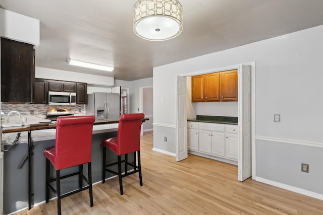 kitchen featuring decorative backsplash, a breakfast bar, stainless steel appliances, and light hardwood / wood-style floors