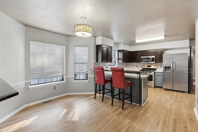 kitchen featuring a breakfast bar, backsplash, appliances with stainless steel finishes, decorative light fixtures, and dark brown cabinetry