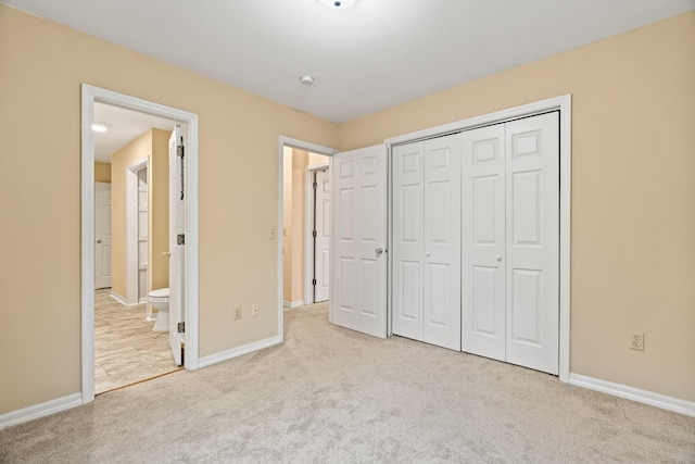 unfurnished bedroom featuring ensuite bath, a closet, and light colored carpet