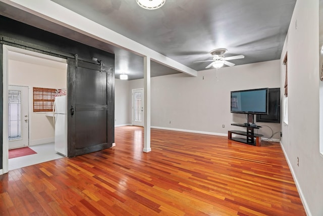 unfurnished living room featuring ceiling fan, a barn door, and light hardwood / wood-style floors