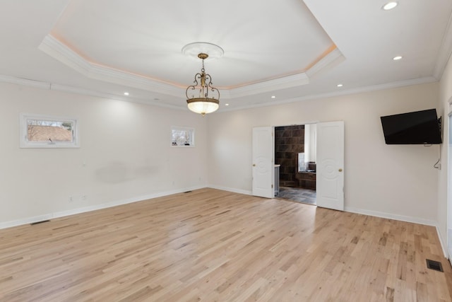 spare room featuring plenty of natural light, a raised ceiling, ornamental molding, and light wood-type flooring