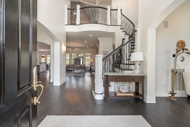 entryway with a notable chandelier, dark wood-type flooring, a towering ceiling, and crown molding