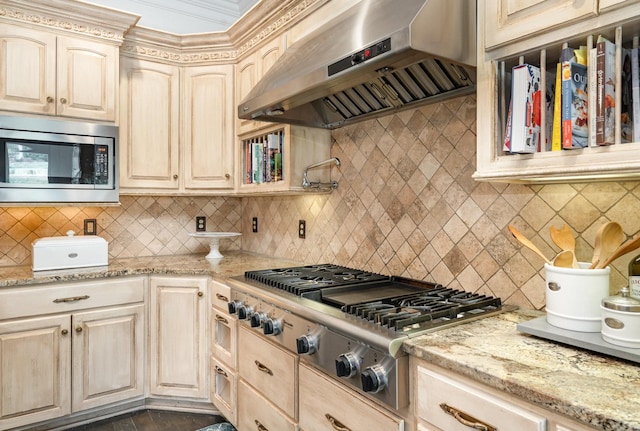 kitchen featuring appliances with stainless steel finishes, light stone countertops, range hood, light brown cabinets, and backsplash