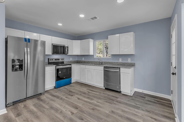 kitchen with sink, white cabinets, light wood-type flooring, light stone countertops, and appliances with stainless steel finishes