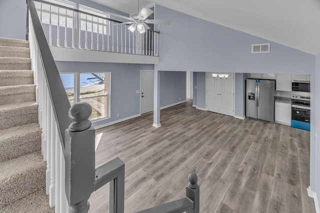 unfurnished living room with light wood-type flooring, high vaulted ceiling, and ceiling fan with notable chandelier