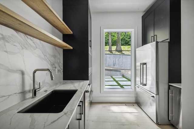 kitchen featuring backsplash, sink, light stone countertops, and stainless steel appliances