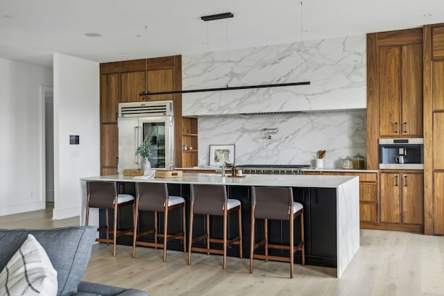 kitchen with sink, an island with sink, appliances with stainless steel finishes, decorative light fixtures, and a kitchen bar