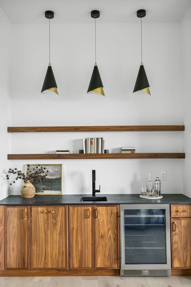 bar with hanging light fixtures, sink, beverage cooler, and light hardwood / wood-style flooring