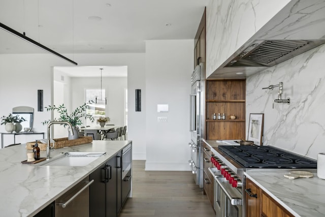 kitchen featuring sink, wall chimney range hood, light stone counters, pendant lighting, and high quality appliances