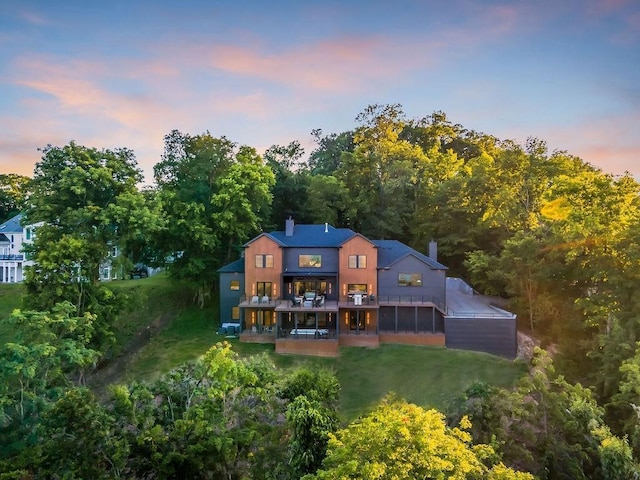 back house at dusk featuring a lawn and a sunroom