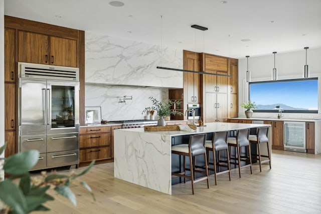 kitchen with a large island, hanging light fixtures, stainless steel appliances, wine cooler, and a breakfast bar