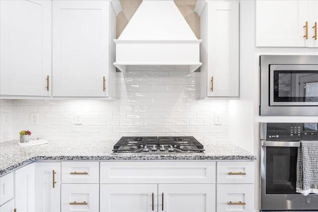 kitchen with white cabinetry, premium range hood, stainless steel appliances, and tasteful backsplash