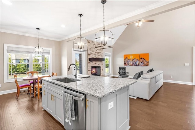 kitchen with sink, light stone counters, stainless steel dishwasher, decorative light fixtures, and a kitchen island with sink