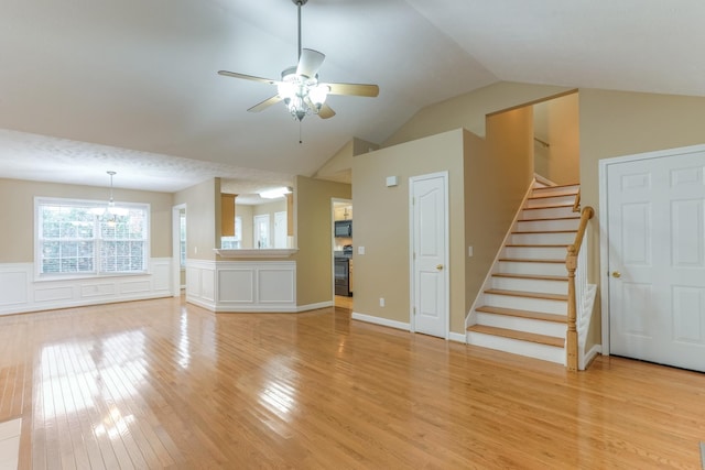 unfurnished living room with vaulted ceiling, ceiling fan with notable chandelier, and light hardwood / wood-style flooring