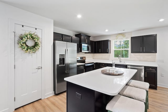 kitchen with a breakfast bar, light hardwood / wood-style flooring, appliances with stainless steel finishes, tasteful backsplash, and a kitchen island