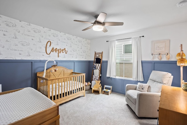 carpeted bedroom featuring ceiling fan and a crib