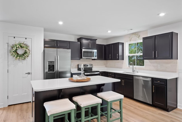 kitchen featuring light wood-type flooring, stainless steel appliances, sink, a center island, and a breakfast bar area