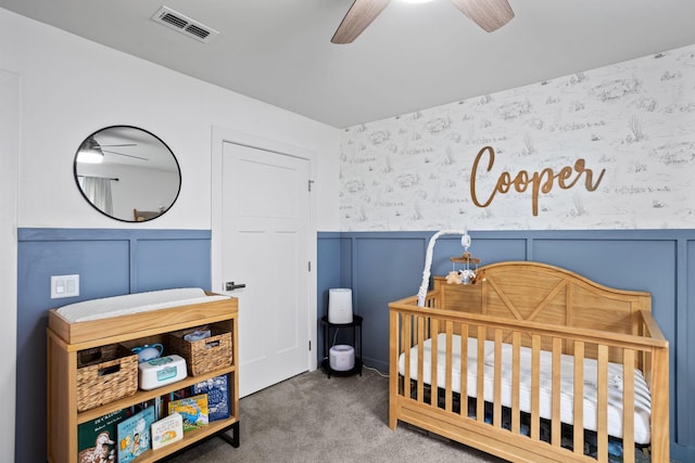 carpeted bedroom featuring ceiling fan and a nursery area