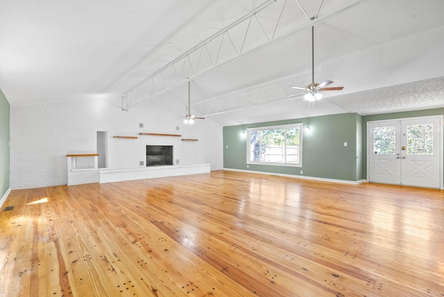 unfurnished living room with french doors, a brick fireplace, ceiling fan, light hardwood / wood-style floors, and brick wall