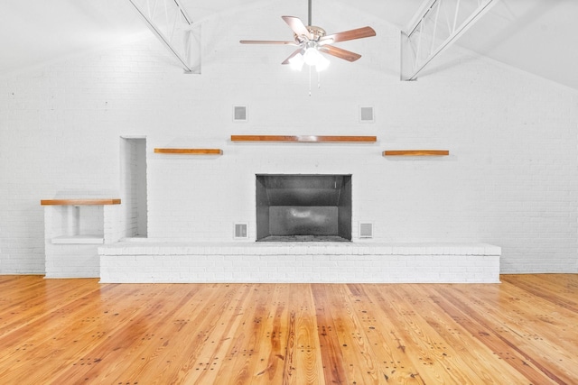 unfurnished living room featuring hardwood / wood-style floors, lofted ceiling, a fireplace, and brick wall