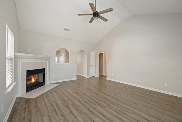 unfurnished living room featuring a tile fireplace, vaulted ceiling, hardwood / wood-style flooring, ceiling fan, and plenty of natural light