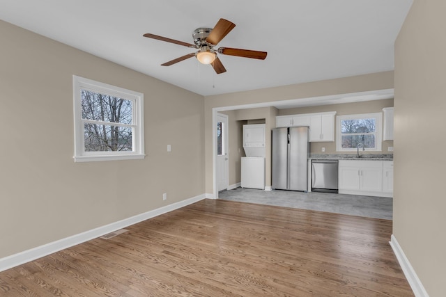 kitchen featuring appliances with stainless steel finishes, white cabinetry, sink, light stone countertops, and light wood-type flooring