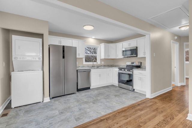 kitchen with white cabinetry, stainless steel appliances, stacked washer and clothes dryer, light stone countertops, and light hardwood / wood-style floors