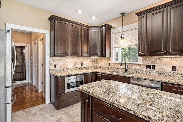 kitchen with light stone countertops, appliances with stainless steel finishes, dark brown cabinetry, sink, and decorative light fixtures