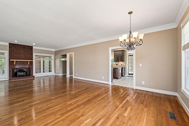 unfurnished living room featuring ornamental molding, light hardwood / wood-style floors, a brick fireplace, and a notable chandelier