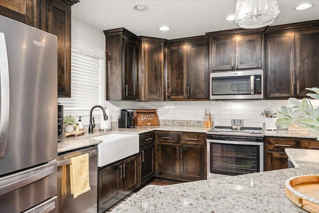 kitchen with dark brown cabinetry, stainless steel appliances, light stone counters, and sink