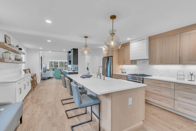 kitchen featuring pendant lighting, a center island with sink, light stone countertops, light hardwood / wood-style floors, and stainless steel appliances